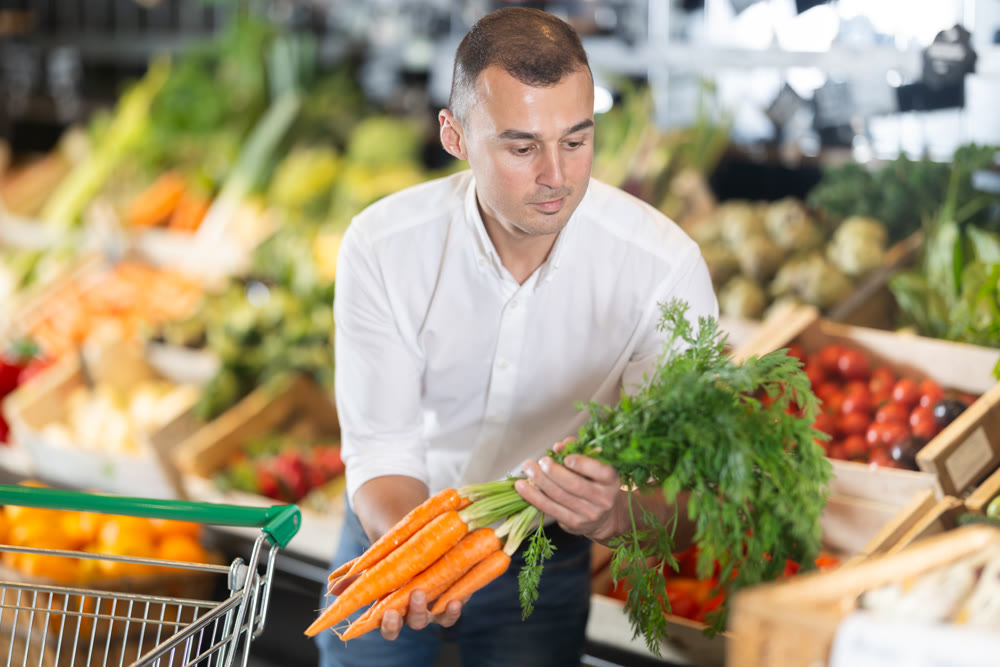 In vegetable department of bio supermarket, male customer took bunch of carrots from window