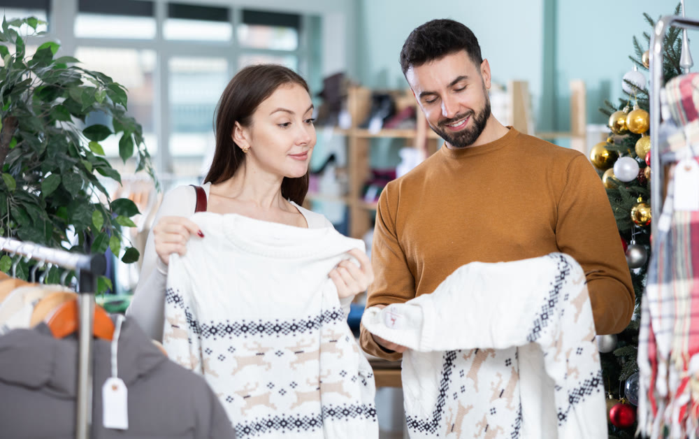 Married couple choose sweaters against background of Christmas tree in clothing store