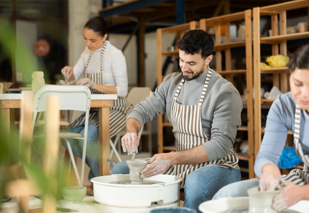 Man in ceramics workshop with pottery wheel and various clay vessels