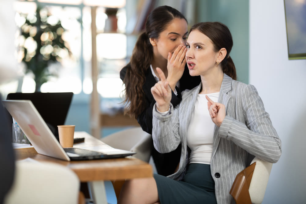 Two female colleagues gossiping in office
