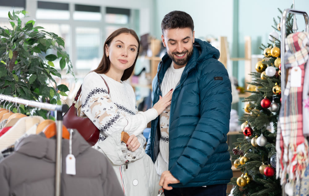 Happy couple examine and selecting clothes for cold season in modern store, man trying new coat