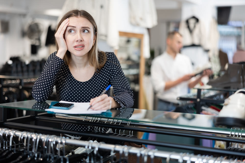 Upset girl store owner make calculations, check documents and counts budget deficit using her phone