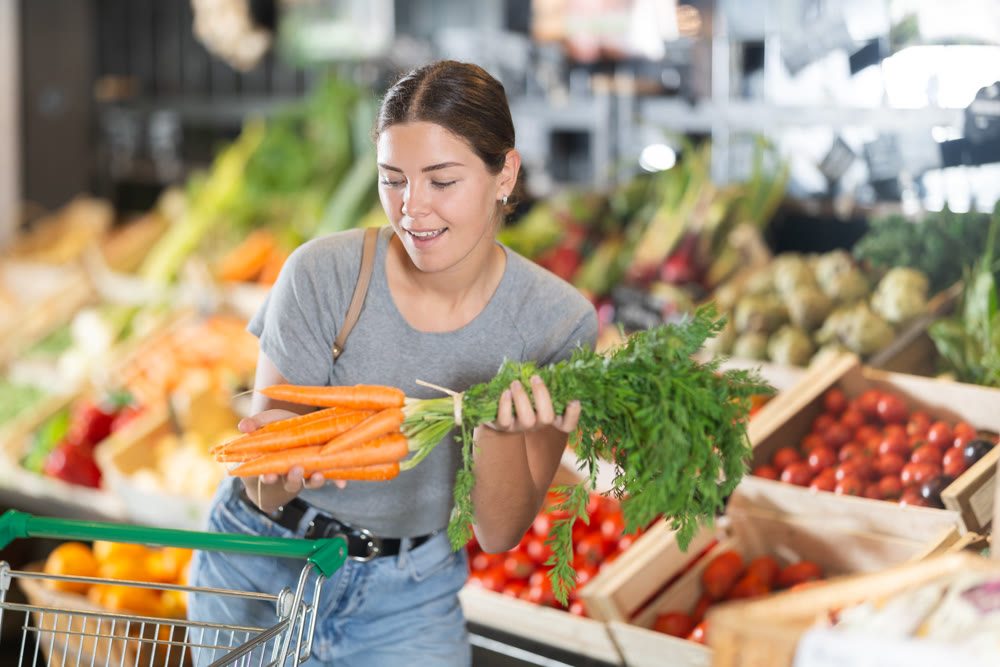 In vegetable department of bio supermarket, female customer took bunch of carrots from window