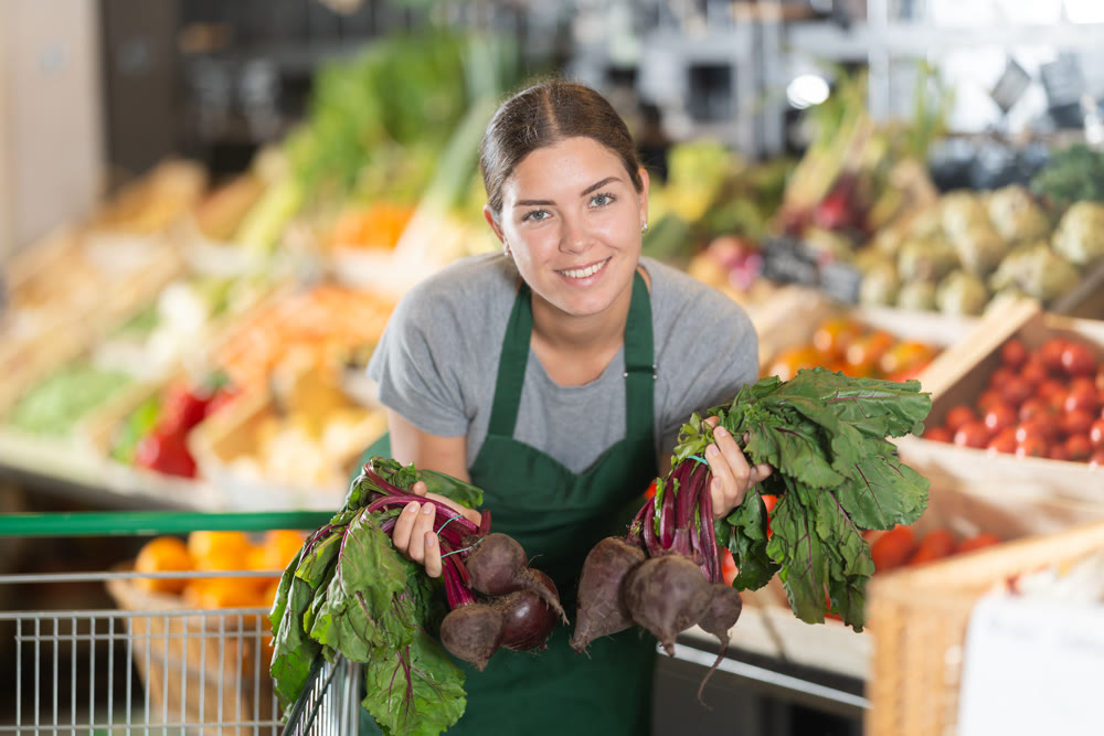 Girl supermarket worker with bunches of beetroots in hands examines product