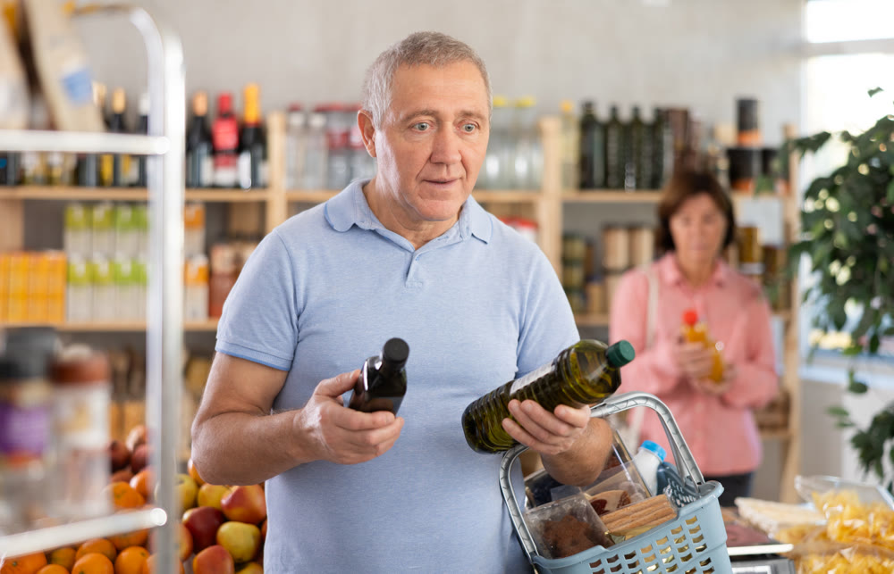 Grocery shopping at supermarket - man chooses olive oil while his wife chooses juice