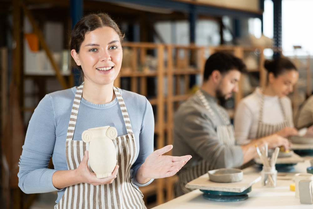 Girl in apron stands with vase in hands, finished clay products from craftsperson