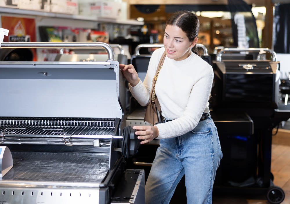 Young woman shopping at garden supermarket - choosing new grill for frying meat