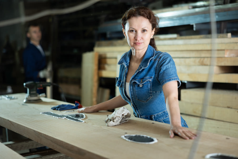 Female sawmill worker cleaning up excess resin or glue on wooden board