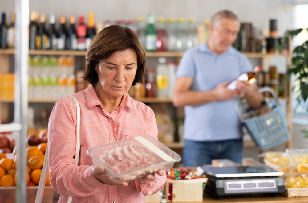 Elderly woman chooses pork in grocery store
