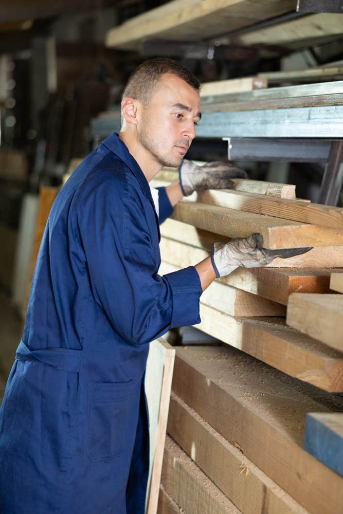 Young man takes oak plank from stack