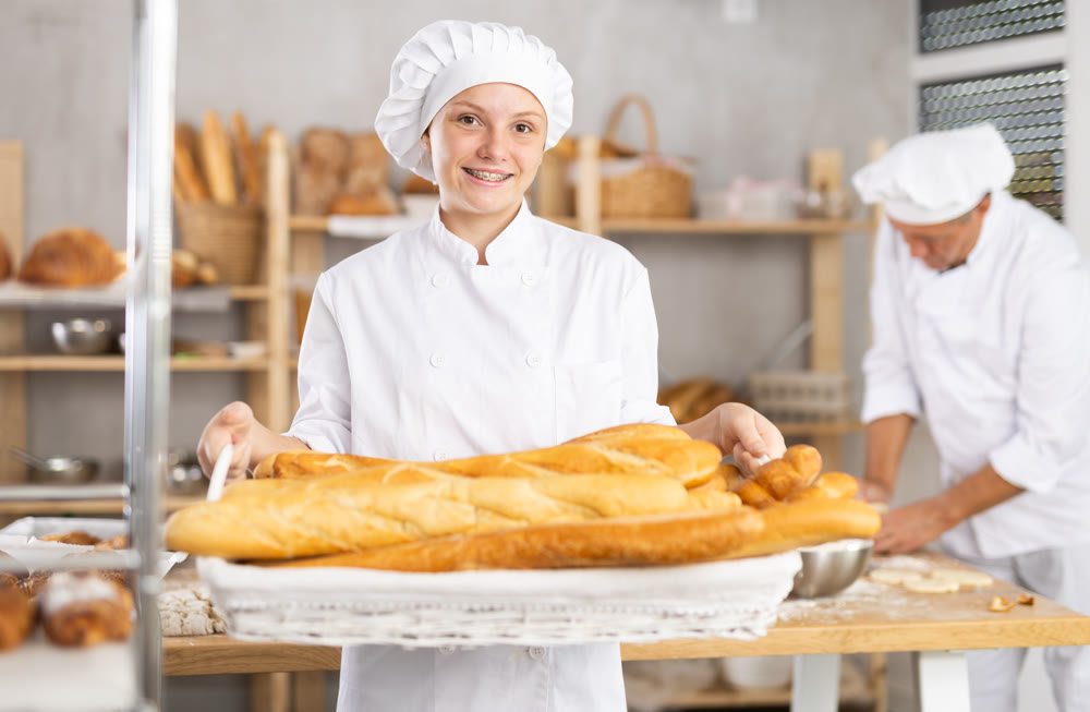 Bakery girl employee holds ready-made baguettes.