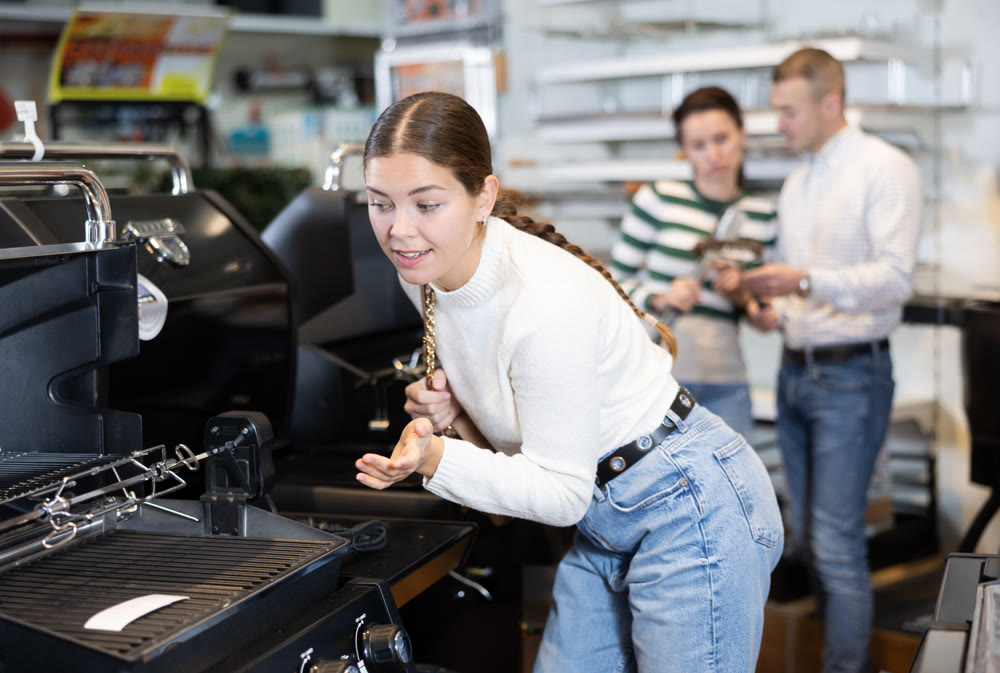 In store, girl inspects mobile grill, buys barbecue device