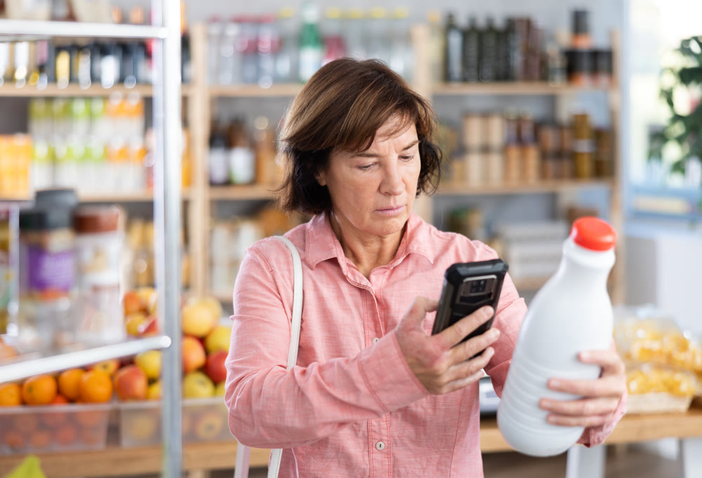 Female buyer checks suitability - scans QR code on bottle of milk label in grocery store