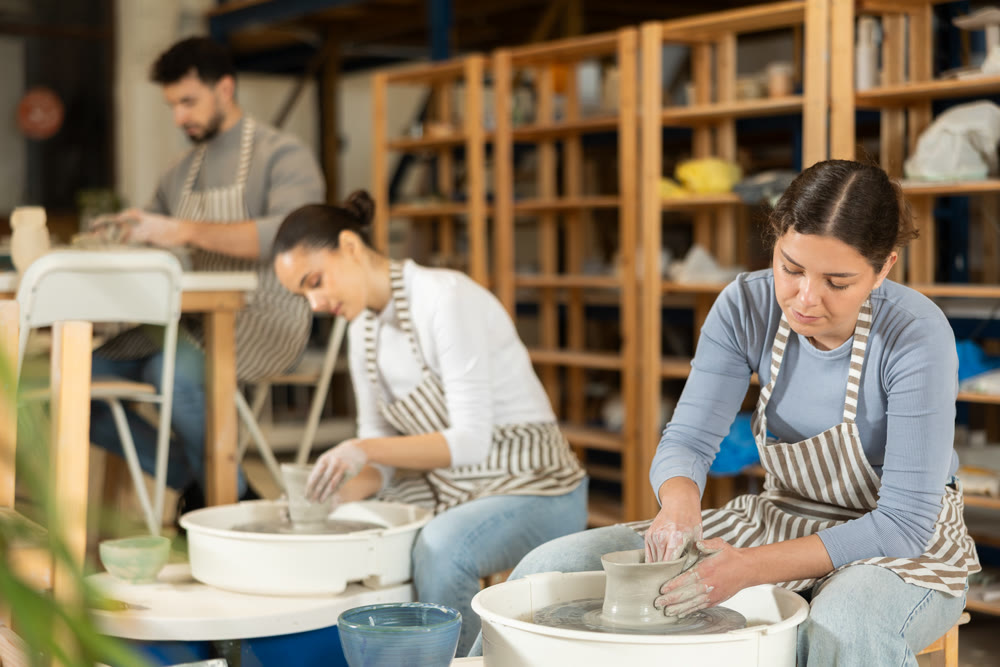 Woman in ceramics workshop with pottery wheel and various clay vessels