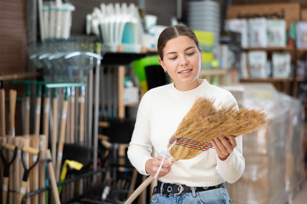 Young woman choosing broom in household store