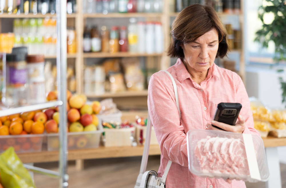 Mature woman is scanning QR on a package of pork in grocery
