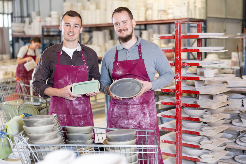 Two men posing with ceramic dishes