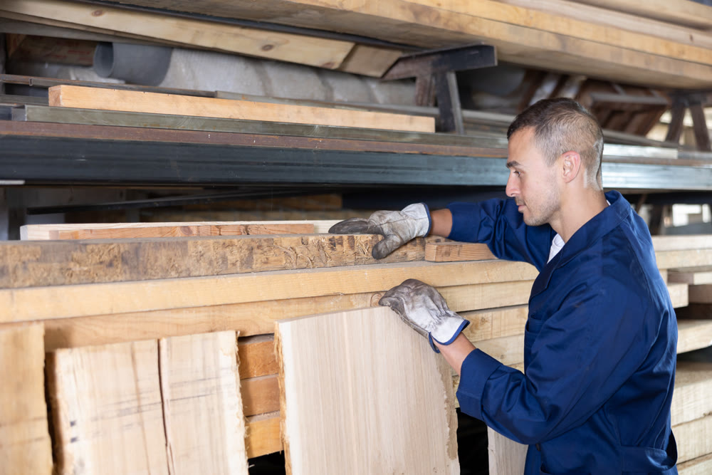 Male sawmill worker stores wooden boards in enterprise warehouse