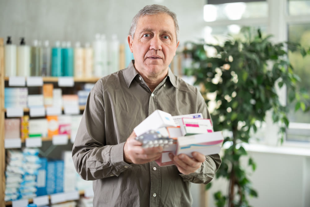 Senior male customer in drugstore with pile of pills.