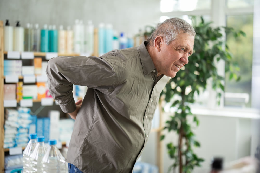 Elderly man holding his back in a pharmacy