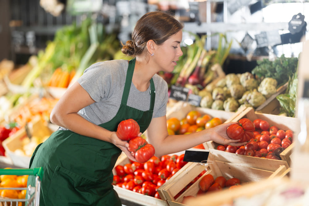 Female vendor organizing ripe tomatoes at farmers market stand