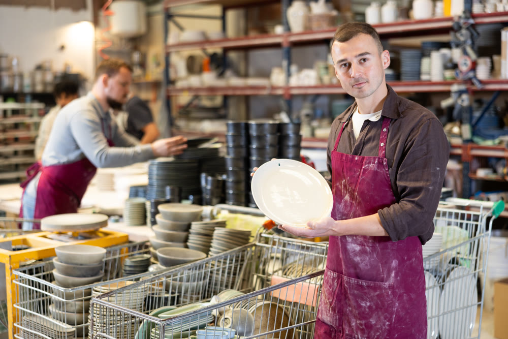 Enthusiastic ceramicist demonstrating handcrafted plates in ceramic studio