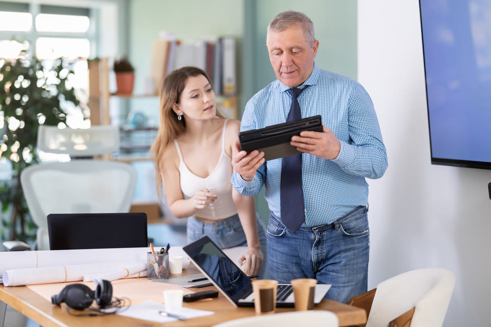 Mature man discussing a new work project with female employee, they look at the tablet