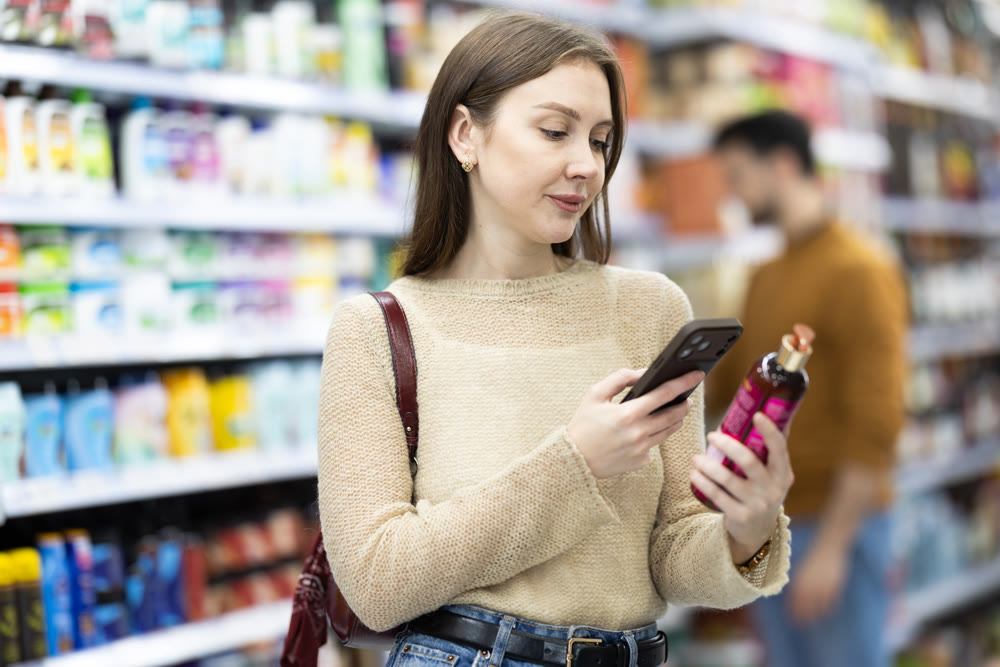 Female buyer scanning qr code for shampoo or shower gel in household chemicals store