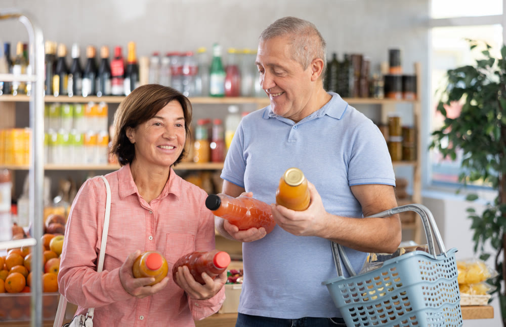 Couple elderly man and woman choosing juices in grocery store