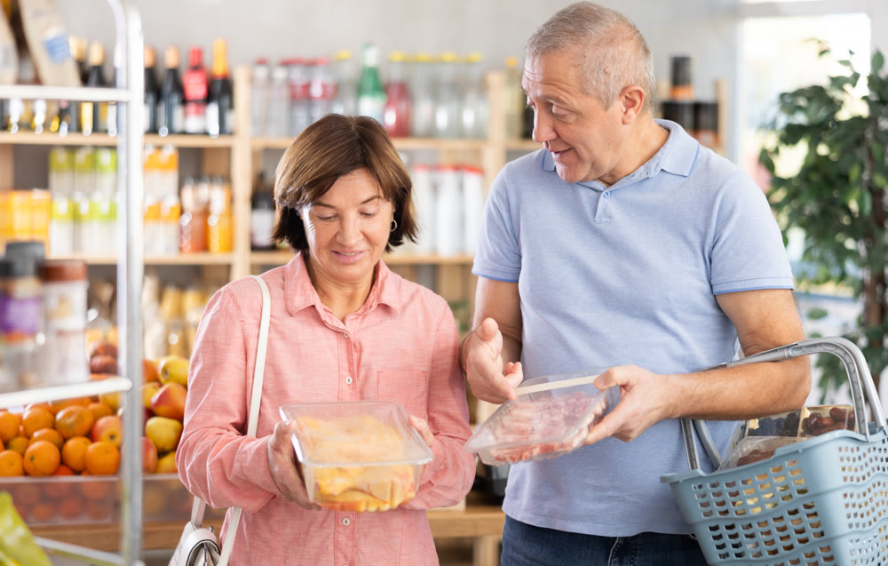 Mature spouses in store took raw chicken and pork meat from shelf, choose meat