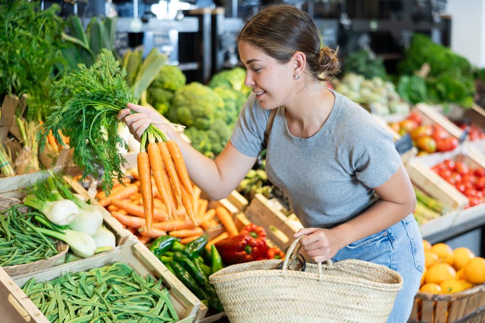 Young girl purchaser buying organic carrot in grocery store