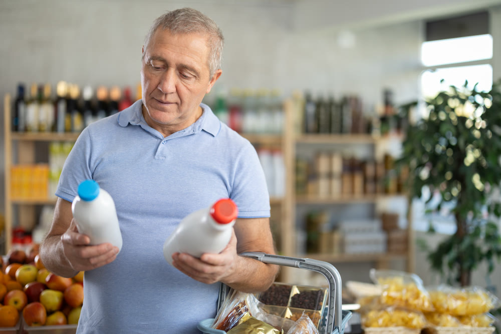 Mature man hold white plastic bottles and choose consider milk in store