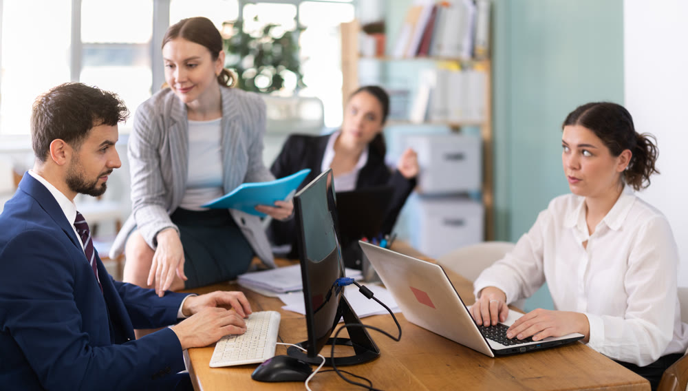 Young woman flirting with male colleague while sitting on office desk