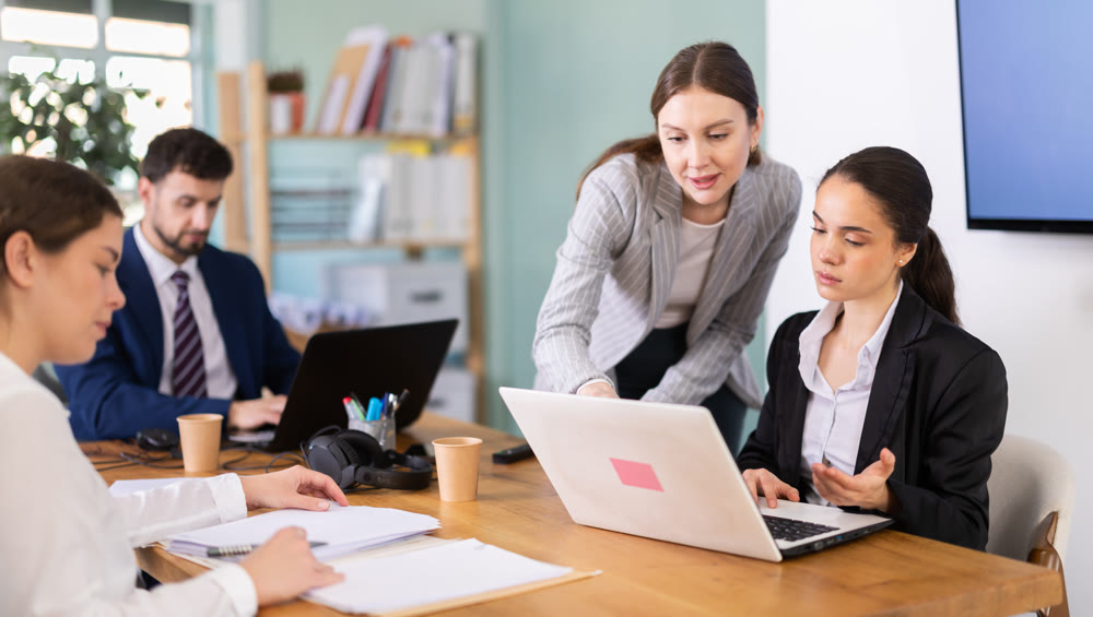 Young girl helping colleague with tasks on laptop