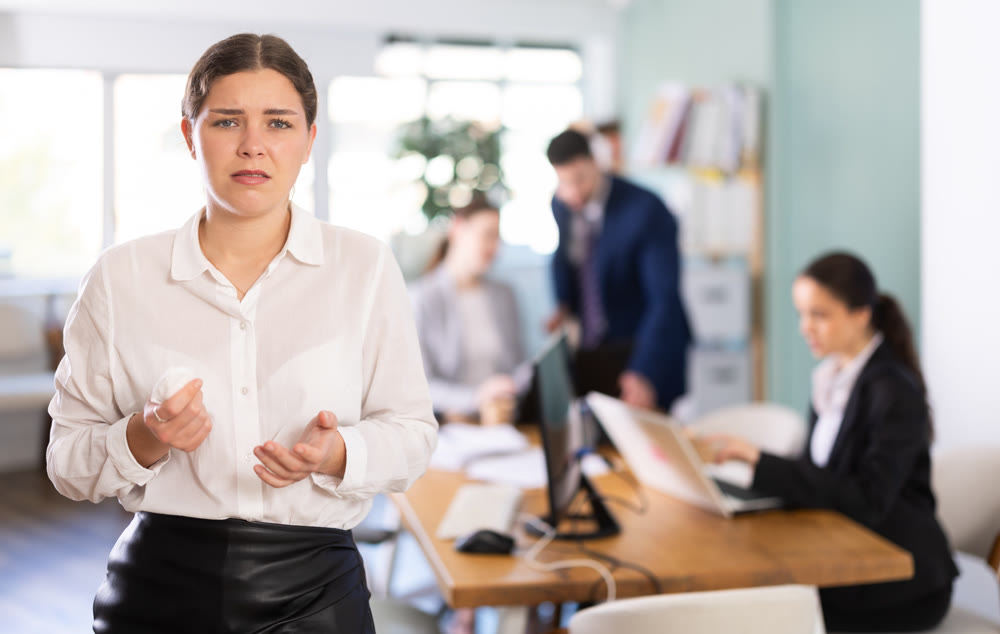 Distressed young woman standing with sad expression in office