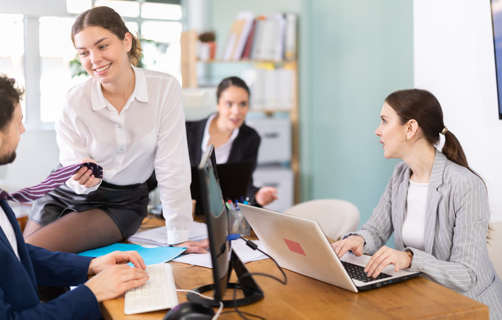 Young woman flirting with male colleague while sitting on office desk