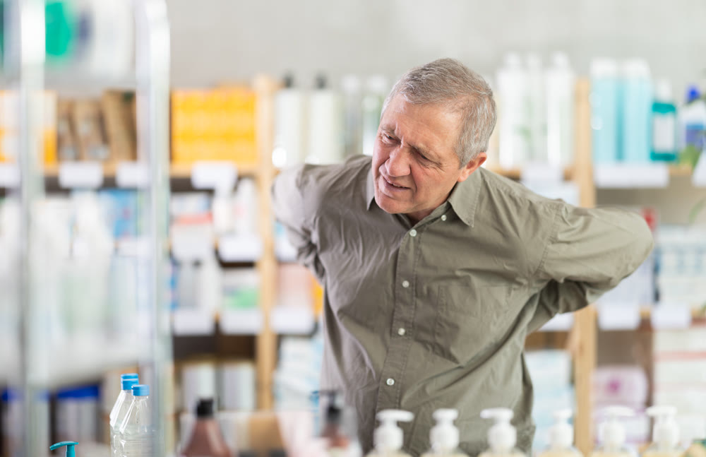 Elderly man holding his back in a pharmacy