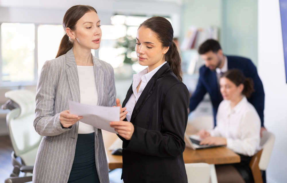 Female colleagues standing and reviewing paper documents in office