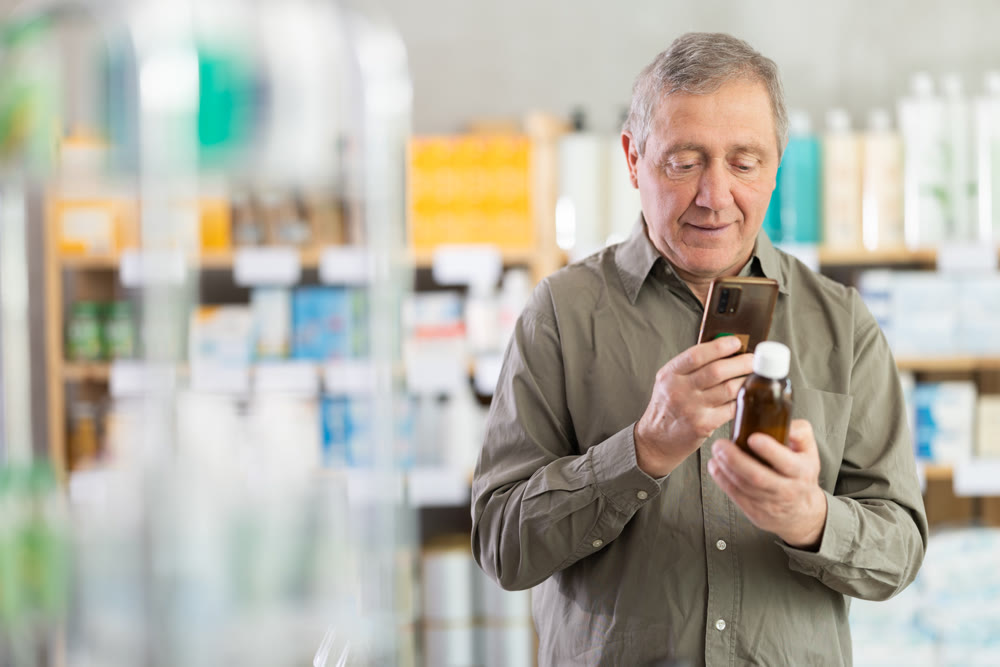 Senior man checking syrup medicine details on smartphone