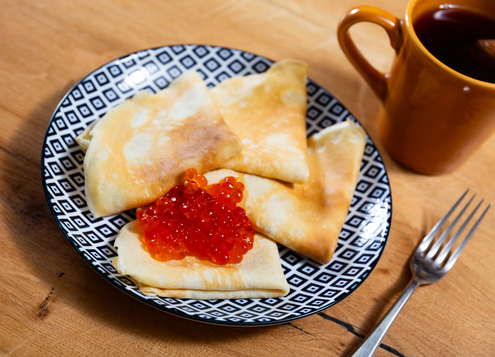 Ruddy pancakes with pile spoonful sturgeon roe. Dish is complemented by cup of tea