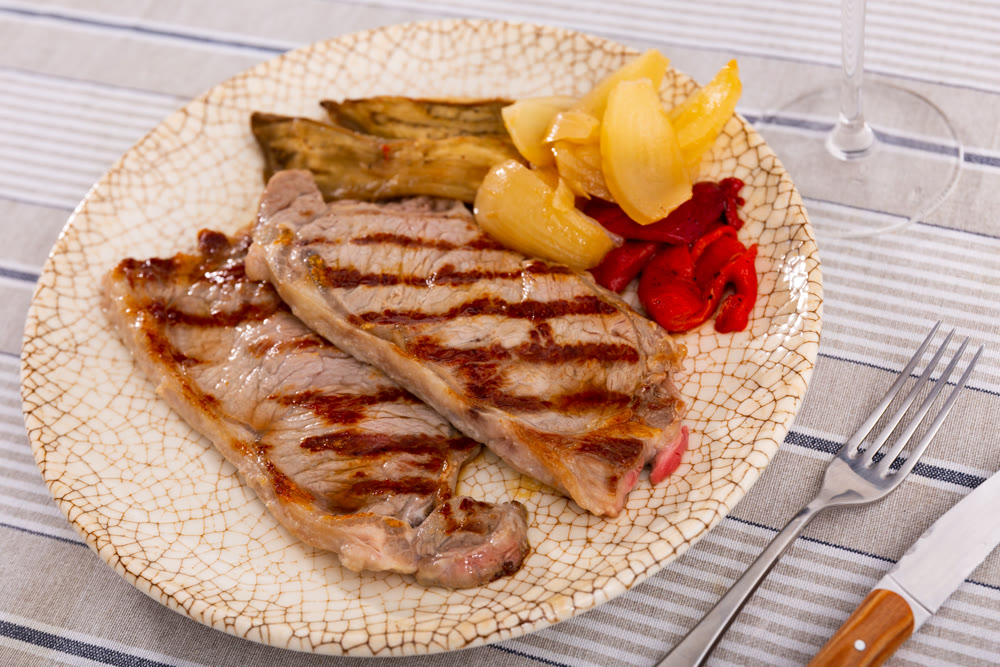 On plate two pieces of barbecue beef with fried vegetables - eggplant slices and green bell peppers