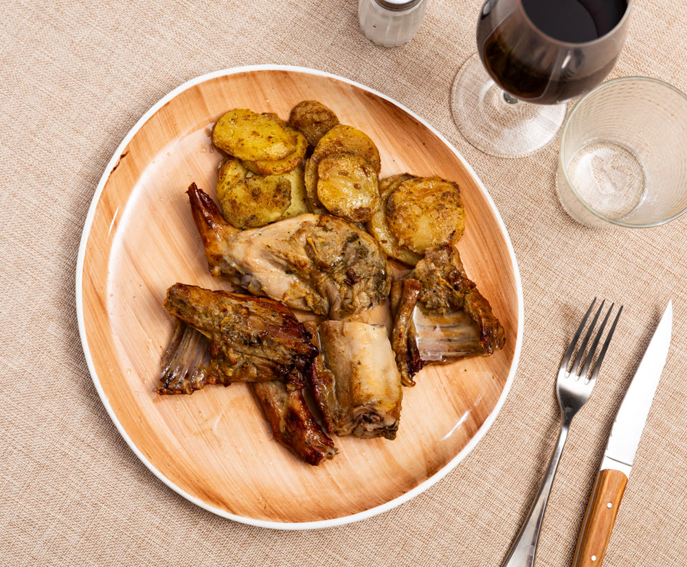 Lunch is served on plate - pieces of young rabbit baked with slice of potato. Close-up