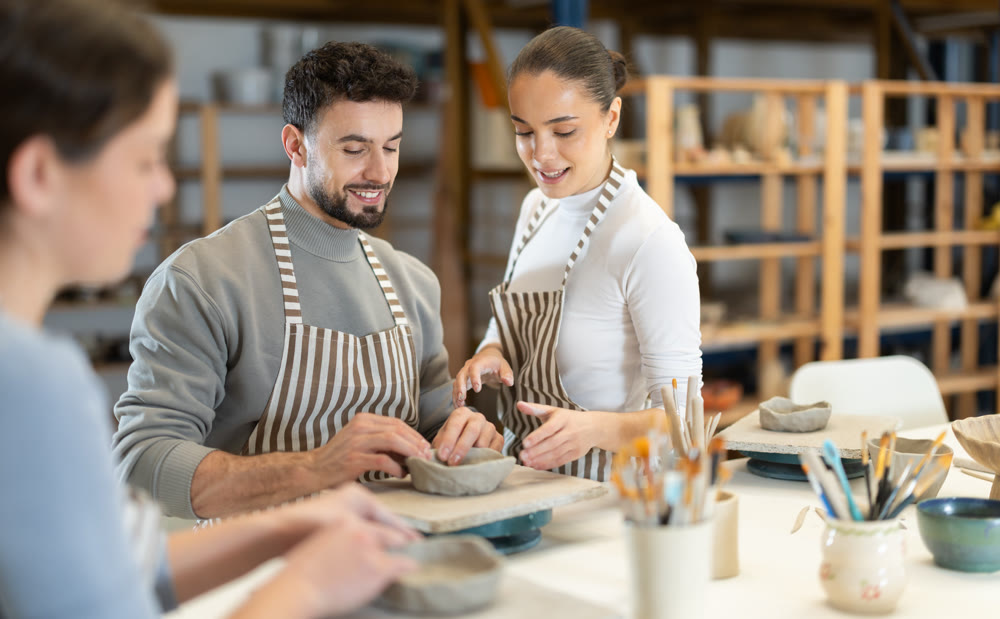 Woman help man sculpting ceramic product from raw clay in workshop