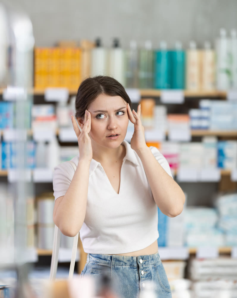 Girl with headache looking for pain relief medicine in pharmacy
