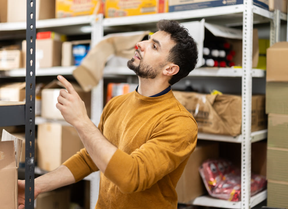 In warehouse, man examines something on shelves, looking for specific box