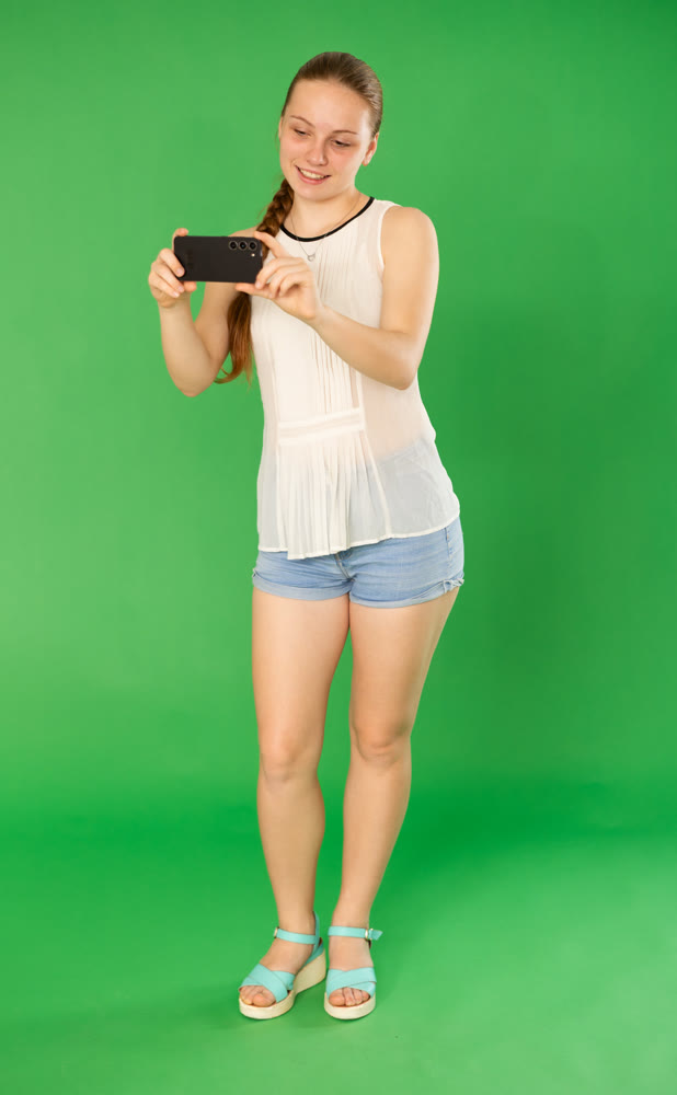 Teenage girl taking photo or scanning QR code in front of green screen