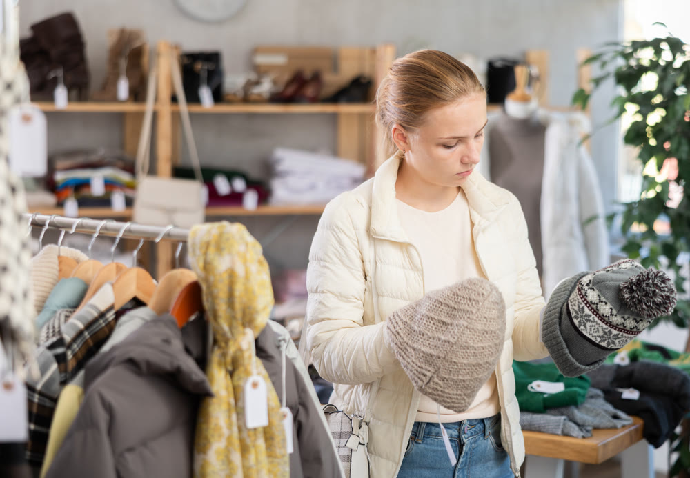 While shopping, girl browsing goods items and choose elect warm hat in store