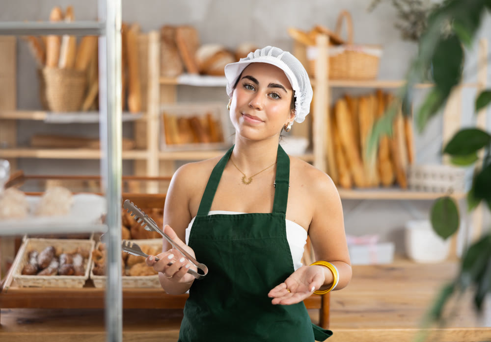 Young woman seller with tongs in bakery