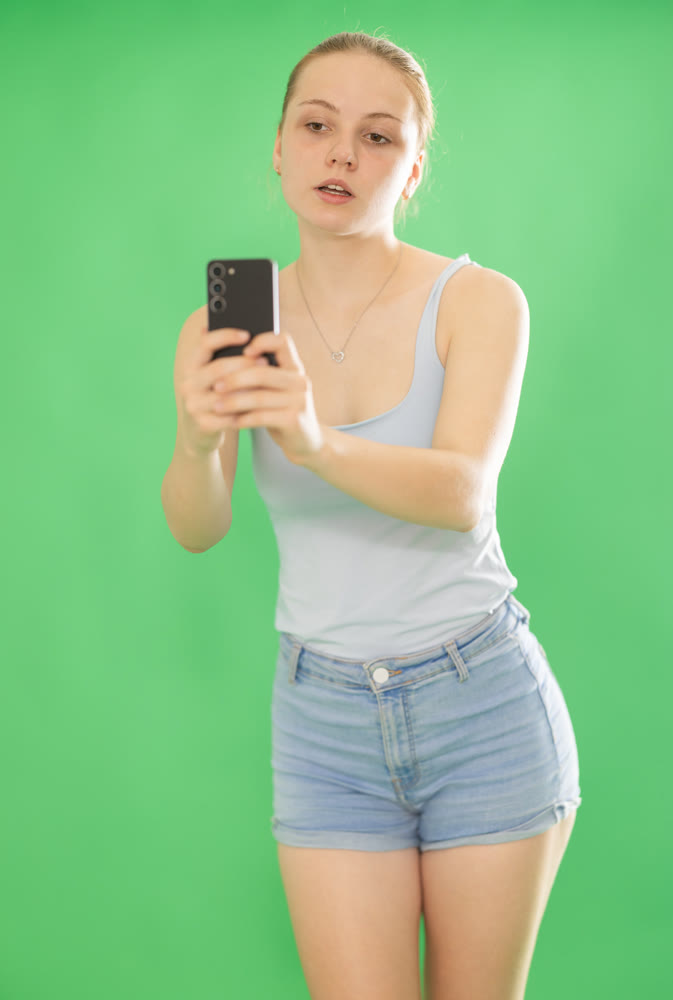 Teenage girl in blue top takes photo or scans QR code with a smartphone. Chroma key compositing