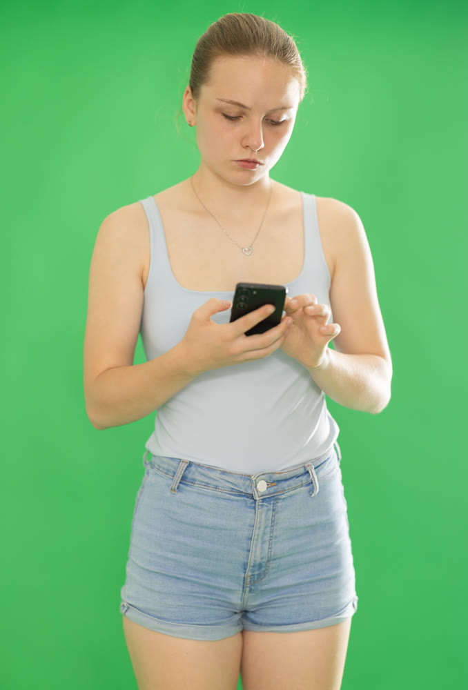 Teenage girl scrolling smartphone in front of green screen